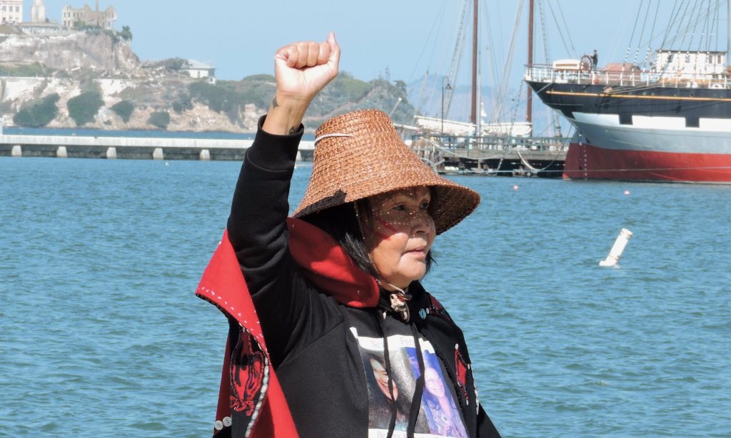 An Indigenous woman raises her fist on Indigenous Peoples’ Day at the first-ever Alcatraz Canoe Journey commemorating 50 years of Indigenous resistance since the 1969 occupation of the once-prison island. (October 14, 2019) Photo by Sarah Manning.